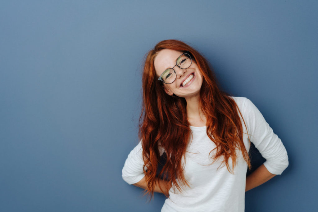 Femme souriante aux cheveux roux contre fond bleu.